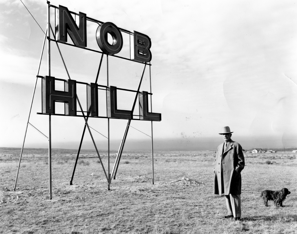 Photo of Colonel D.K.B. Sellers in front of Nob Hill sign with dog on the empty east mesa. Photo from Albuquerque Museum collection circa 1940.