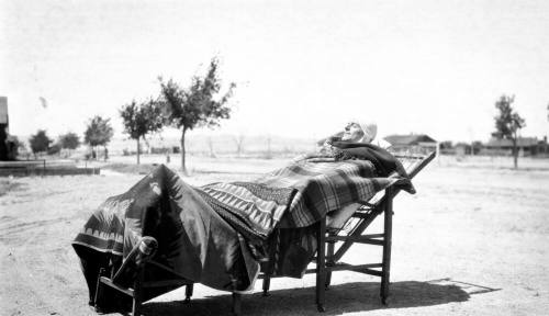Person lounging outdoors covered with blanket and in hat for TB treatment.